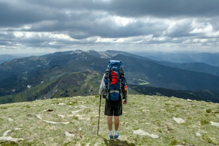 Man with backpack hiking on Hoverla Mountain in Ukraine. Cloudy skies and scenic view create a sense of adventure.