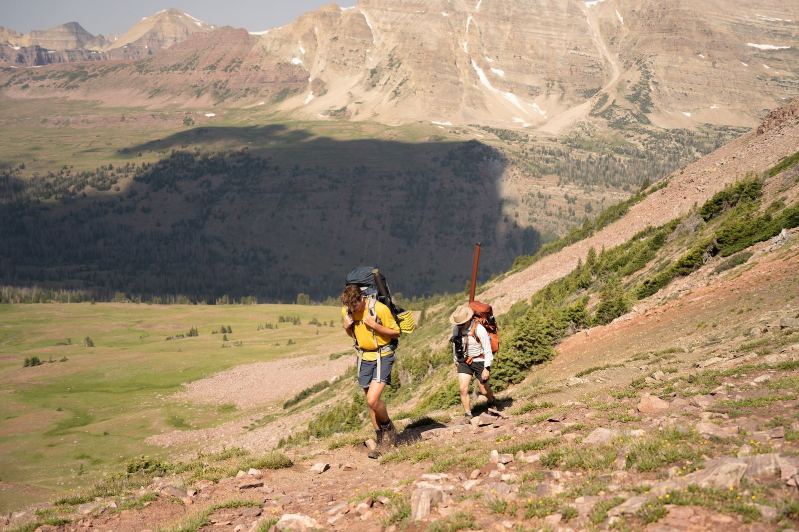 Two hikers ascend a trail in Utah's scenic Uinta Mountains under clear skies.