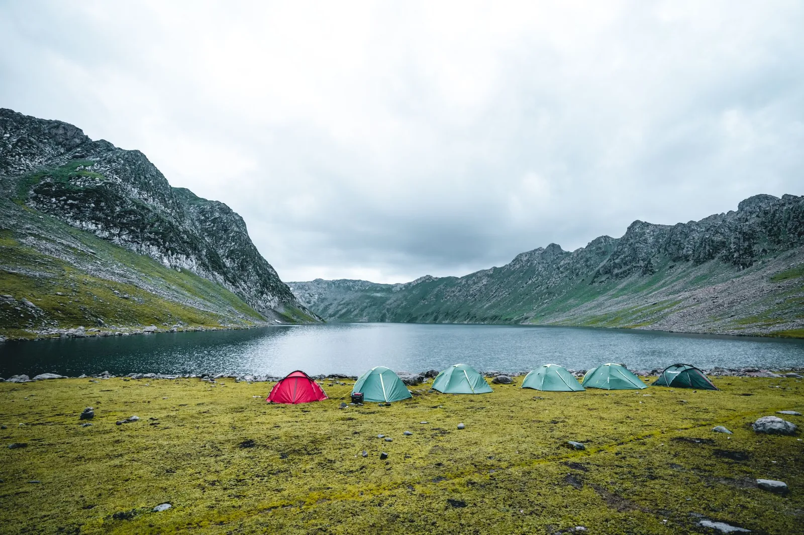 A serene mountain campsite with tents overlooking a calm lake under cloudy skies – ultralight gear evaluation