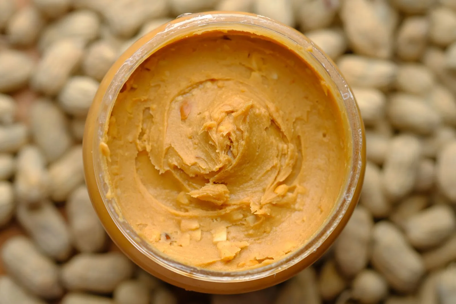 Peanut butter in a glass jar with peanuts
